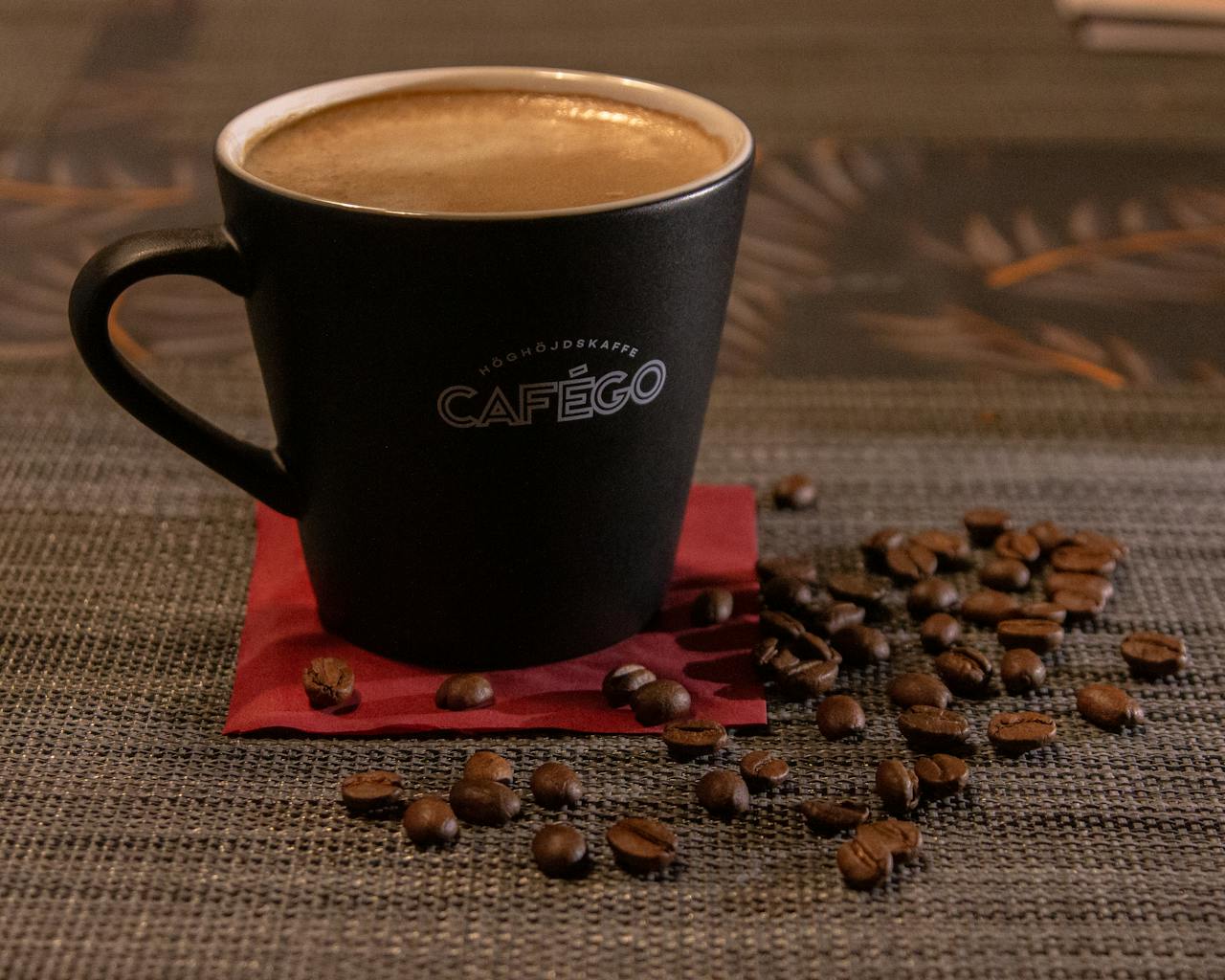 contact-img Cafego coffee mug filled with espresso surrounded by coffee beans on textured surface.
