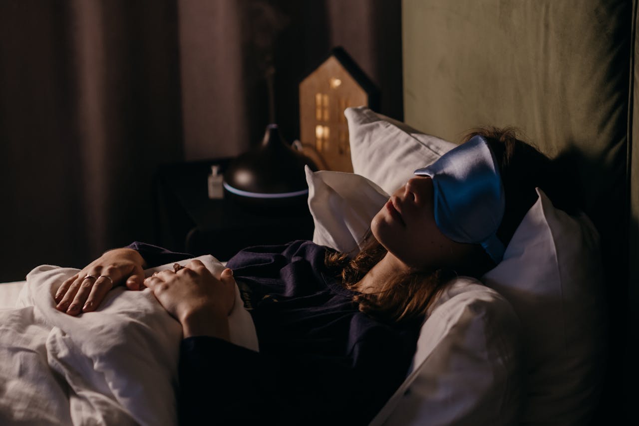 hero-img-01 A woman resting with a sleep mask in a calm bedroom setting, creating a serene and cozy atmosphere.