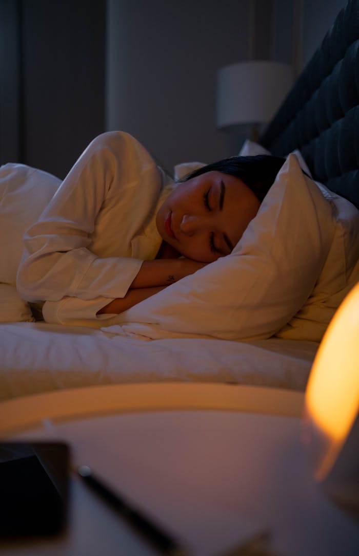 gallery-5 A peaceful woman rests in a serene bedroom environment, lit softly by a bedside lamp.