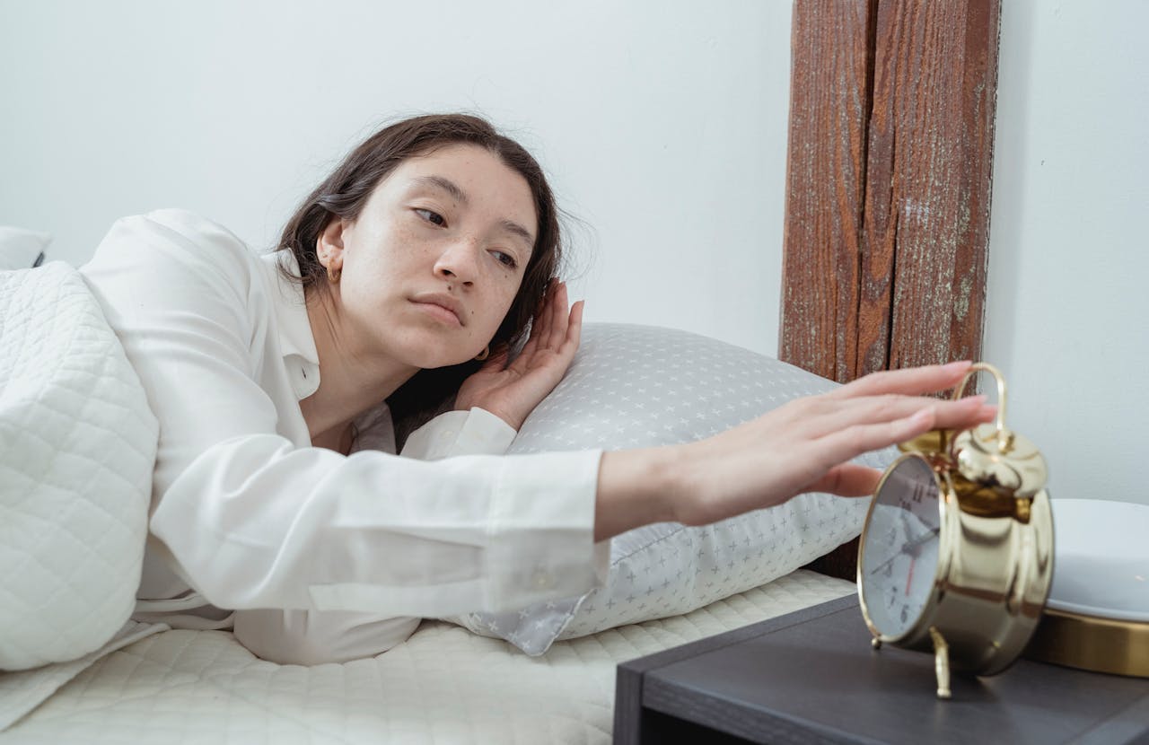 gallery-4 Sleepy young brunette female in white sleepwear resting in comfortable bed and waking up with alarm clock at home in morning time